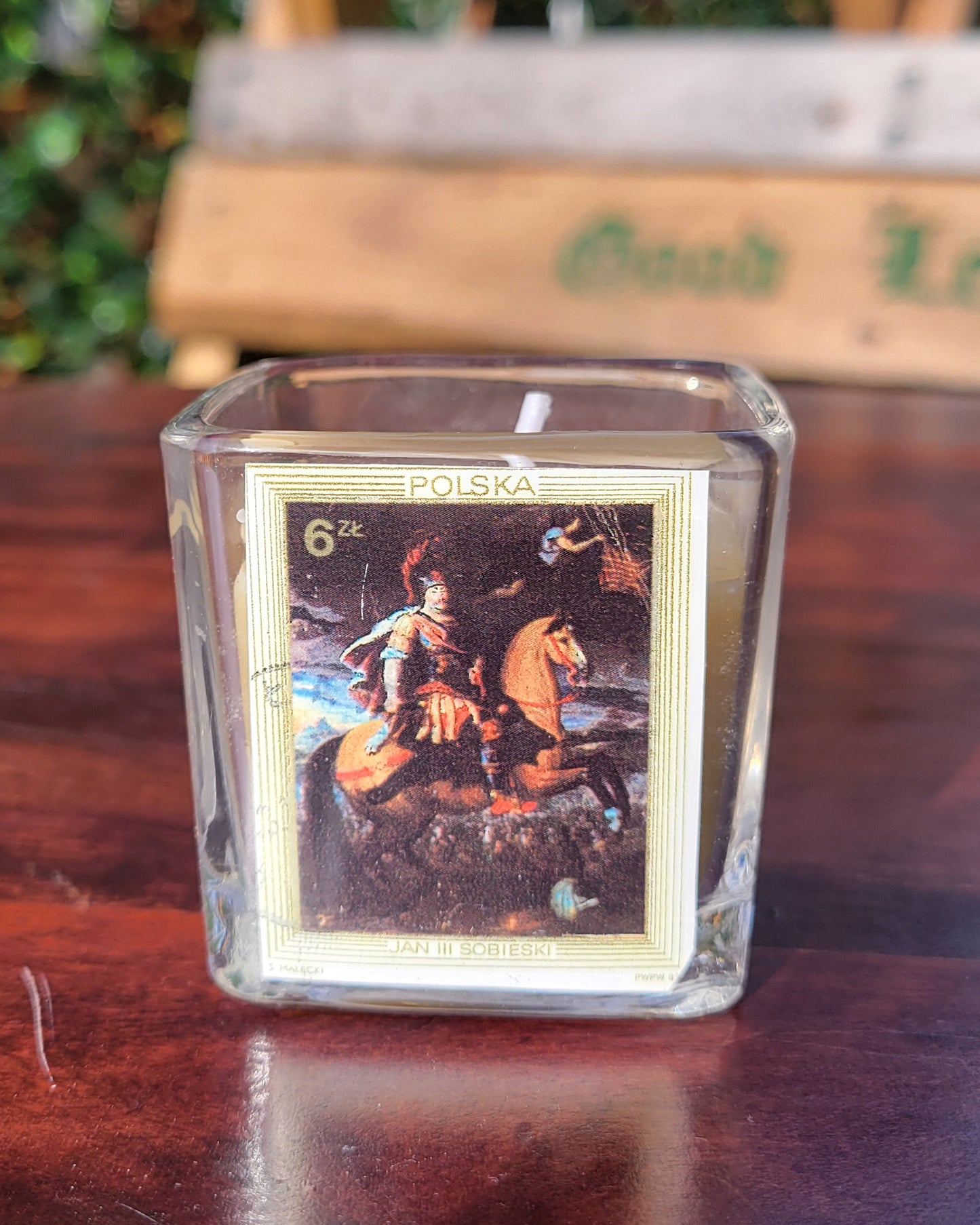 Glass candle with a printed design of a person on a horse, labeled 'Polska', on a wooden surface.