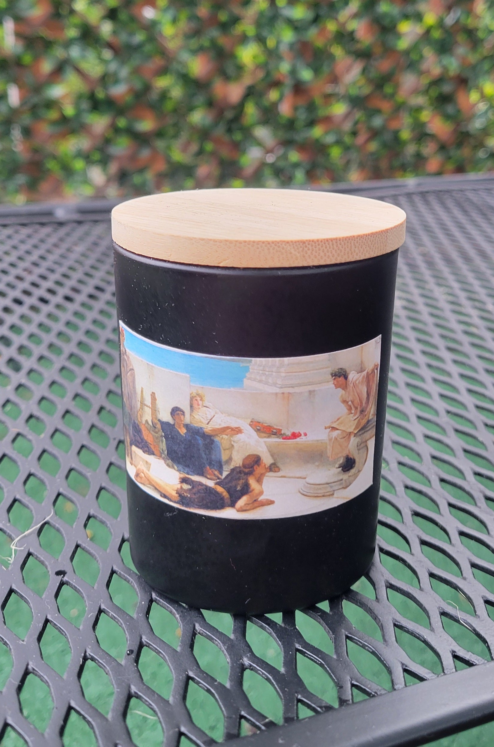 A giftable candle with a design of a classical painting, A Reading From Homer, on the front. 